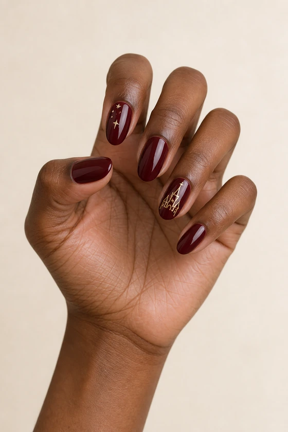 Deep brown hand with glossy burgundy almond nails, gold castle art, and tiny gold stars in soft daylight