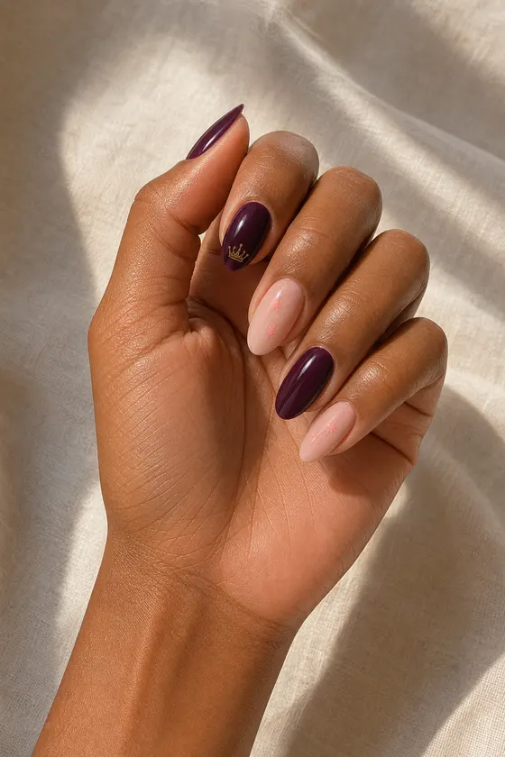 Medium-deep warm brown hand with glossy deep plum and blush nude medium soft almond nails, one tiny gold crown and blush-pink starbursts, a gentle curled pose, bare wrist, short partial forearm, and natural daylight