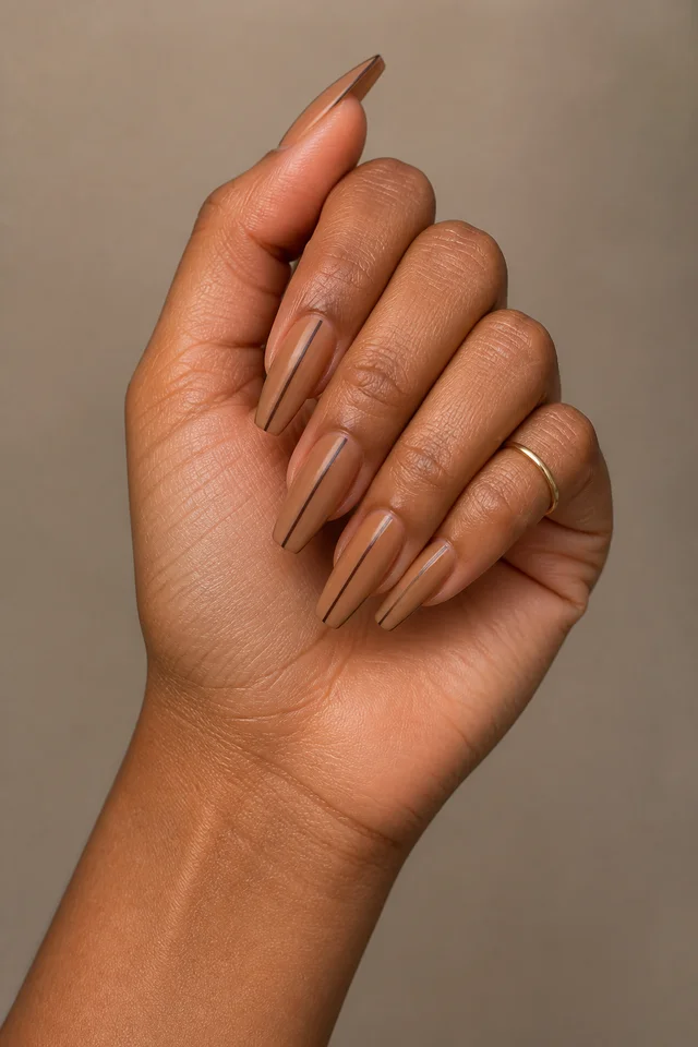 Espresso fine-line coffin nails on a softly curled hand with medium brown skin and a beige quilted cuff in natural daylight