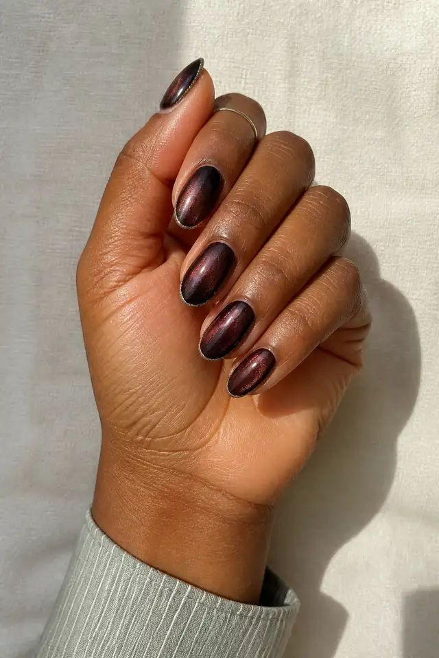 Black cherry velvet nails with silver glitter edges on medium almond tips, tan skin, and a curled hand pose in natural daylight
