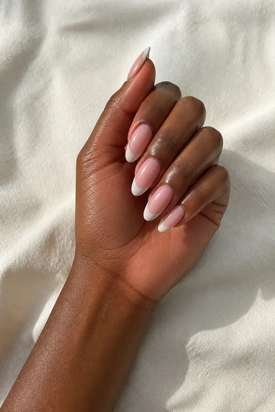 Deep brown skin hand in a softly curled pose with rosy beige pearl oval nude nails and neutral fabric beneath