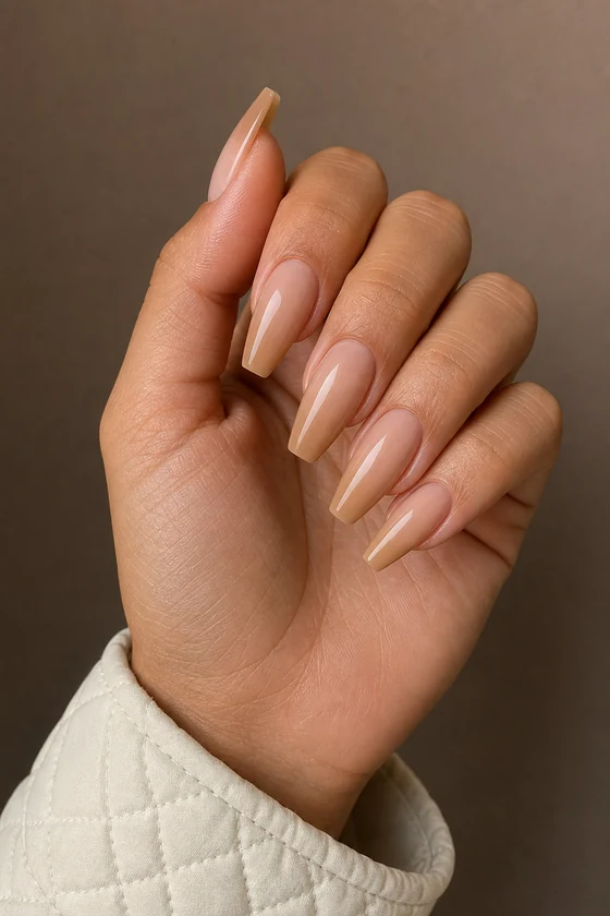Medium tan skin hand in a compact curled pose wearing glossy warm beige almond nude nails with a white quilted cuff