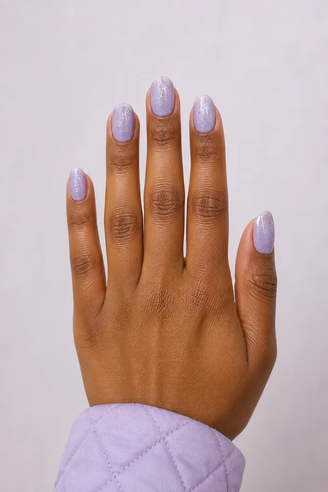 Creamy lavender short almond nails with fine silver sparkle on one rich brown skin tone hand in a controlled upright narrow fan with a lavender quilted cuff and connected short wrist
