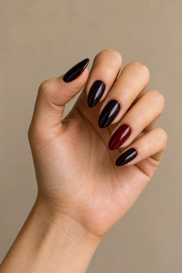 Black cherry glossy almond nails with one deep garnet accent, a controlled curled display pose, light olive skin, and a bare wrist in natural daylight