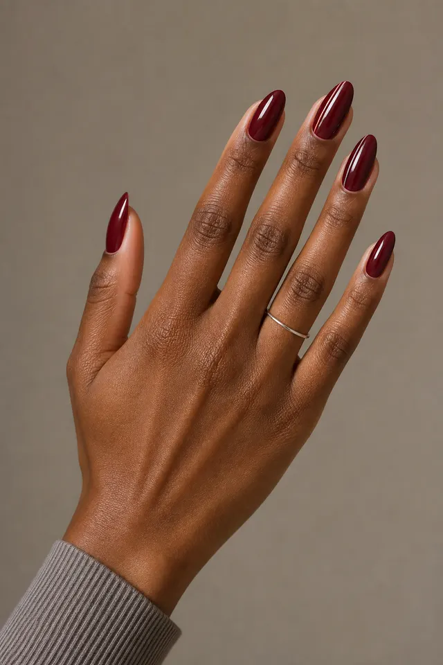 Rich wine glossy French nails with a burgundy side stripe on long almond nails, an open diagonal display pose, rich dark brown skin, a narrow stripe sleeve, and one tiny silver ring in natural daylight