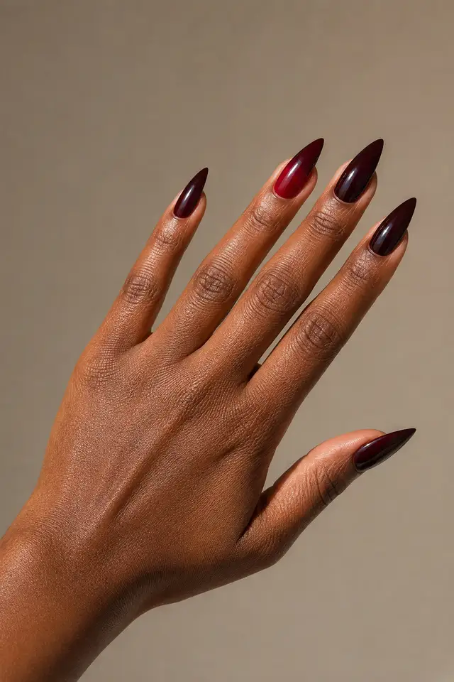 Glossy near-black cherry red stiletto nails with one rich red accent on one rich dark brown skin tone hand, shown in an upright open diagonal display with a connected wrist