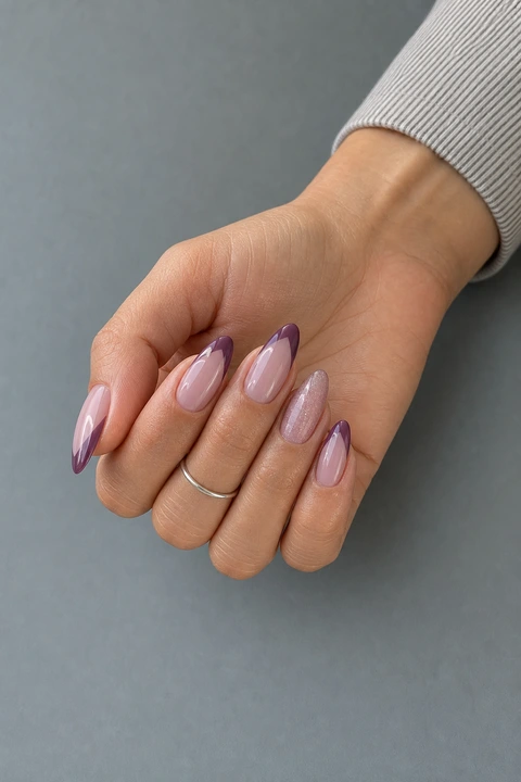 Glossy mauve-plum V French long almond nails with an icy shimmer accent on a light-olive hand in a softly curled pose with a muted striped cuff and tiny silver ring in natural daylight