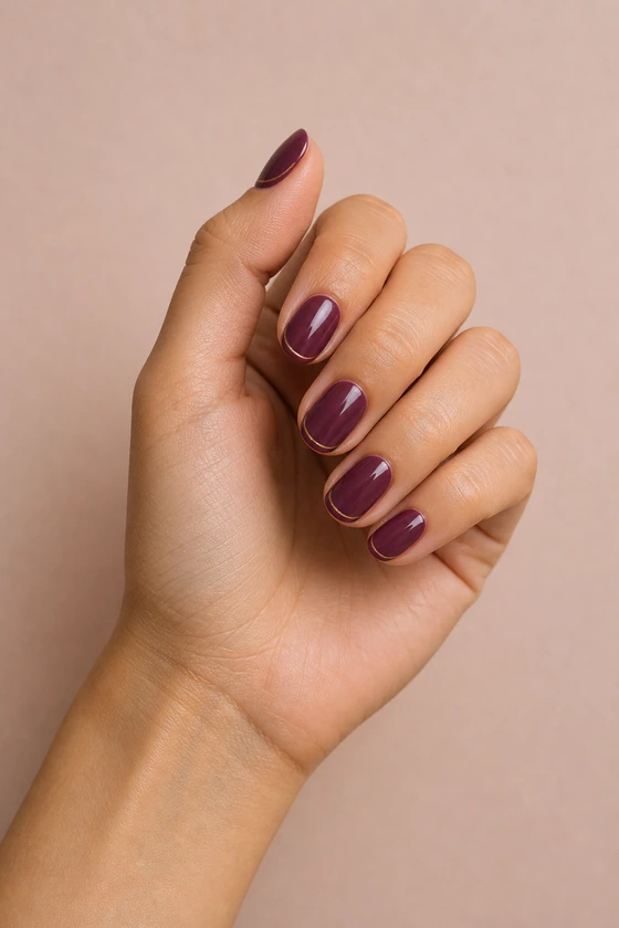 Light olive skin hand in a relaxed curled pose wearing short glossy berry-plum oval nails with fine muted-gold edge lines
