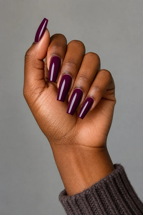 Glossy deep plum long coffin acrylic nails with straight sidewalls and flat tips on rich dark brown skin in an upright softly curled pose with a taupe knit sleeve, visible short wrist, and natural daylight