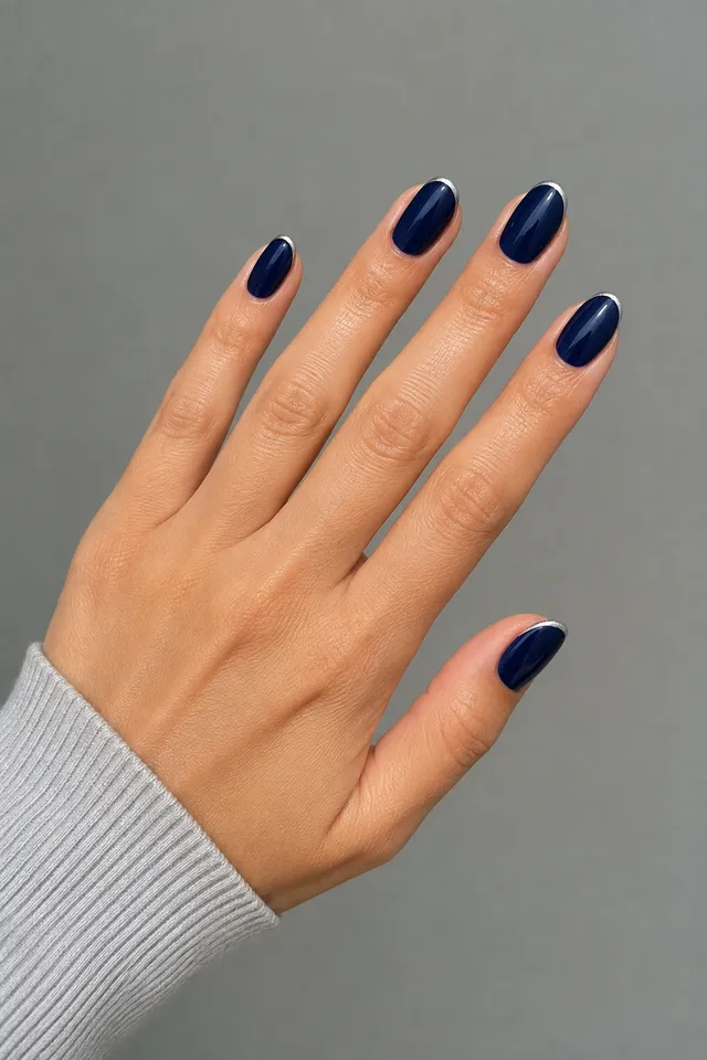 Glossy deep navy short almond nails with ultra-fine silver edges on one light olive skin tone hand in a relaxed diagonal five-finger fan with a pale grey narrow-stripe cuff and connected short wrist