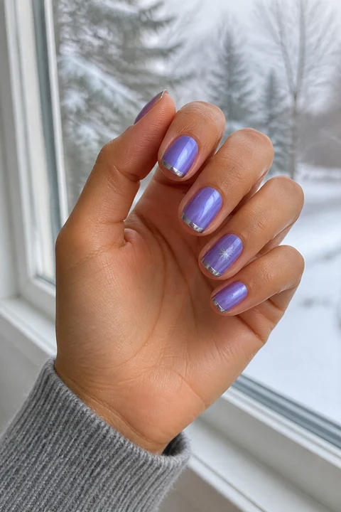 Glossy lavender chrome short rounded-square nails with narrow silver French edges and one icy star on tan warm skin in an upright softly curled pose with a grey knit sleeve, visible short wrist, and natural daylight